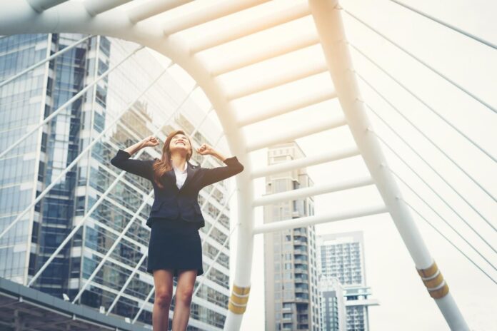 happy-success-businesswoman-overlooking-into-city-center-hands-raised
