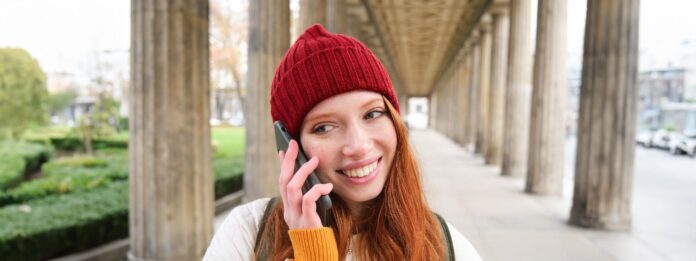 smiling-cute-redhead-woman-makes-phone-call-holds-telephone-near-year-has-mobile-conversation